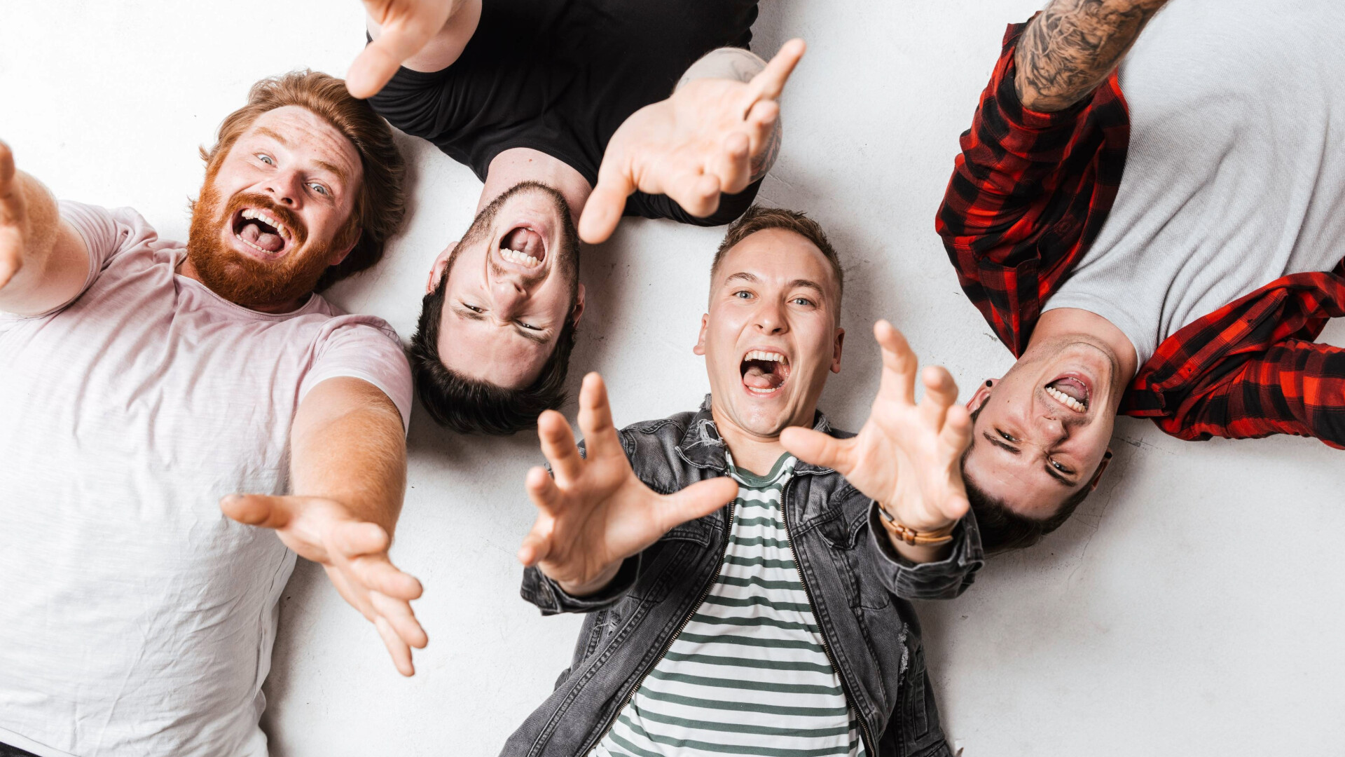 Die Band liegen Kopf an Kopf am Rücken und strecken die Hände nach oben