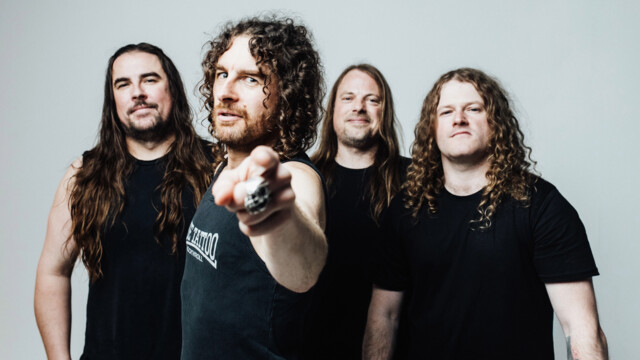 Airbourne vor einer weißen Wand. Sänger Joel O'Keeffe zeigt in die Kamera.