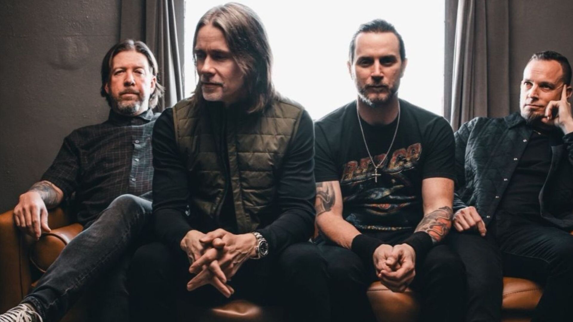 Die Band Alter Bridge sitzt auf einer braunen Couch vor einem Fenster