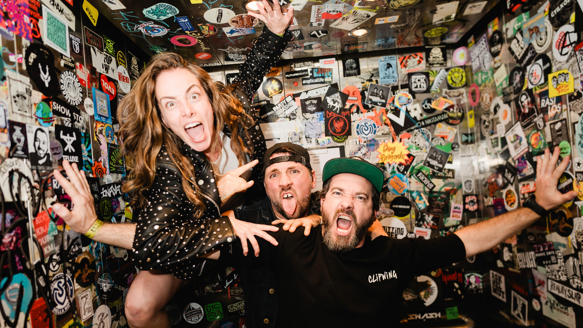 Die Band posiert in einem engen Raum voller Sticker