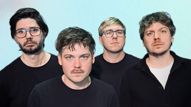 Band steht in schwarzen Outfits vor hellblauem Hintergrund