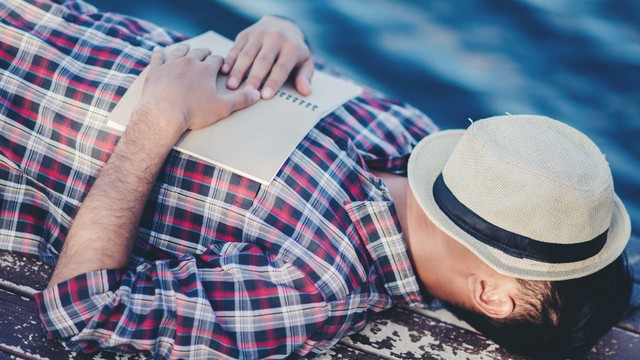 Ein Mann liegt und schläft mit Hut über dem Gesicht