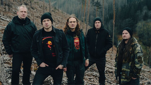 Die Band steht auf einer Steigung, dahinter ist ein Wald zu sehen