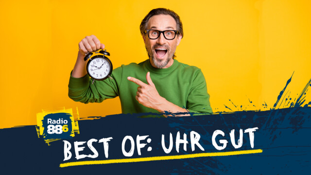 Ein Mann mit grünem Pulli und Brille, hält in der rechten Hand einen Wecker