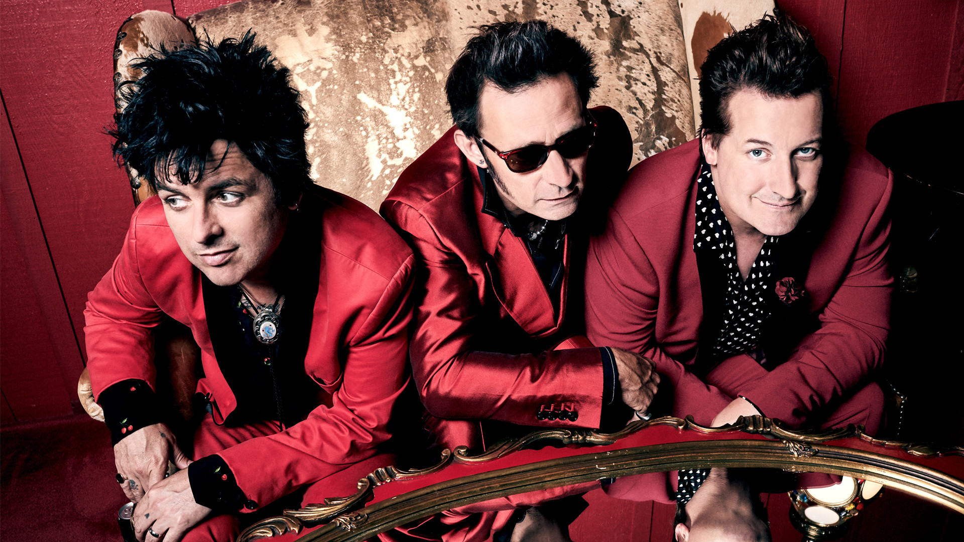 Greenday ©.Warner Music Bandfoto von Greenday in roten Anzügen auf einem Sofa