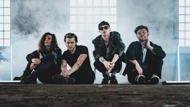 Die Band sitzt in Nebelschwaden in einer Industriehalle